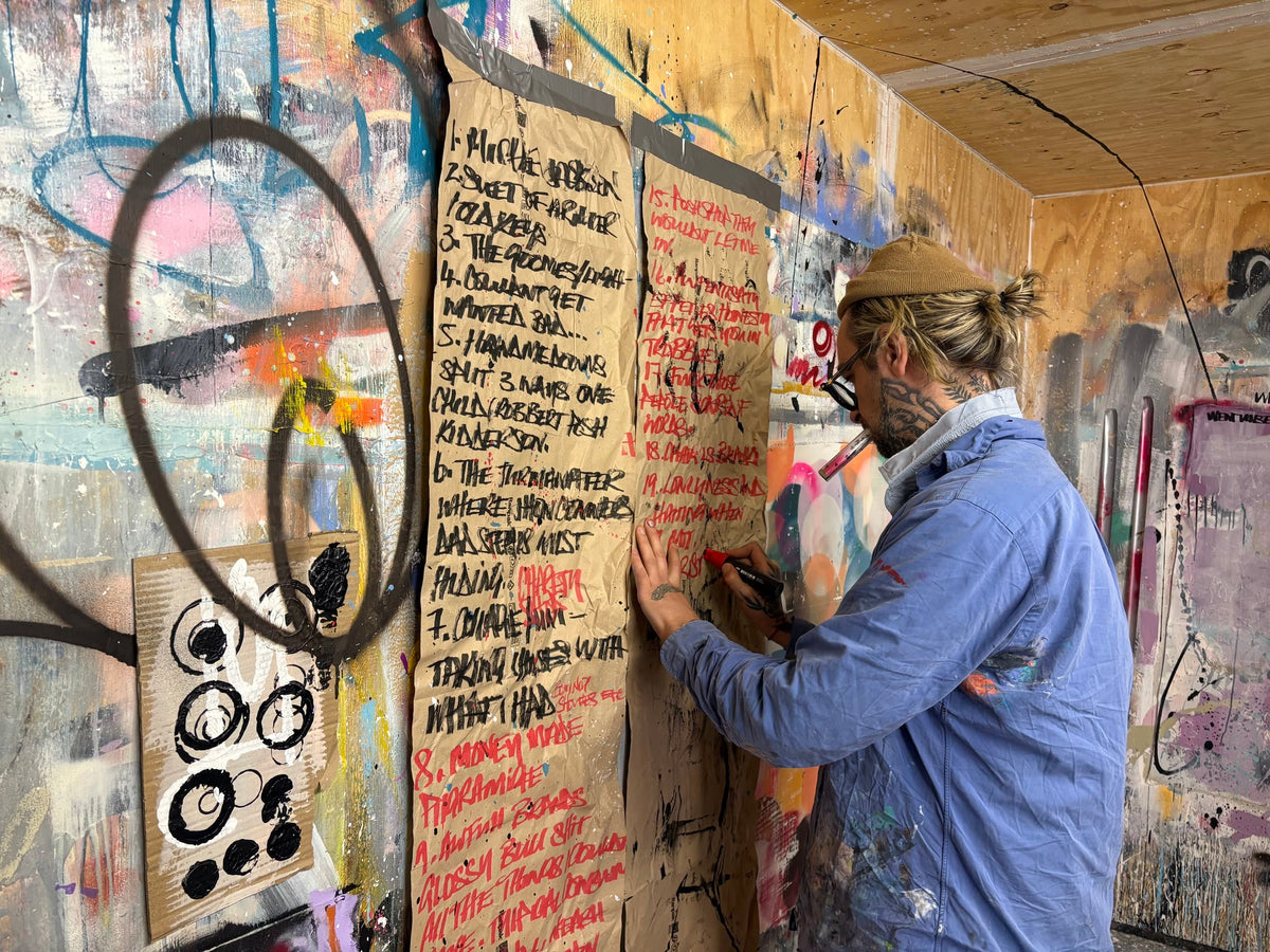 Joseph Gilgun writing in red marker on sheets of brown paper taped to a painted studio wall
